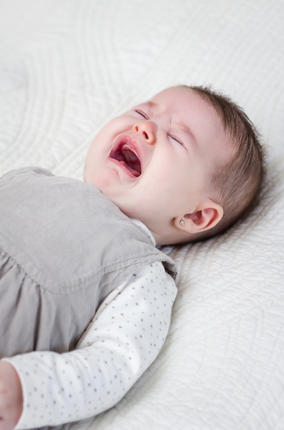 Baby girl crying over white bedcover