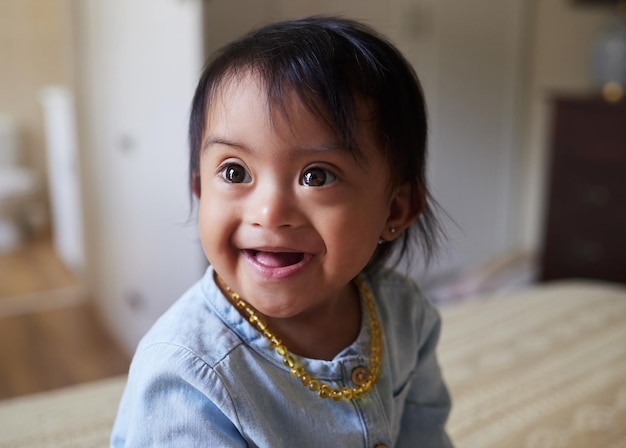 Baby girl and cute with a down syndrome little child on a bed in the bedroom of her home alone Children kids and face with a sweet female kid looking innocent pure and carefree in her house