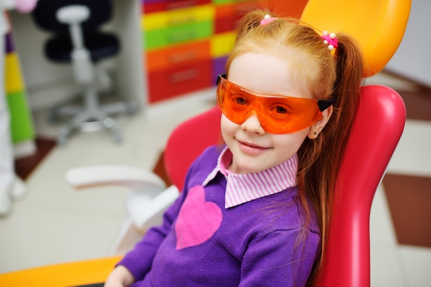 Baby girl in dental glasses smiling sitting in dental chair.