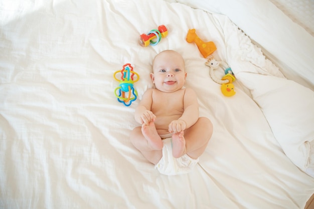 Baby girl in a diaper lying on the bed with toys rattles top view