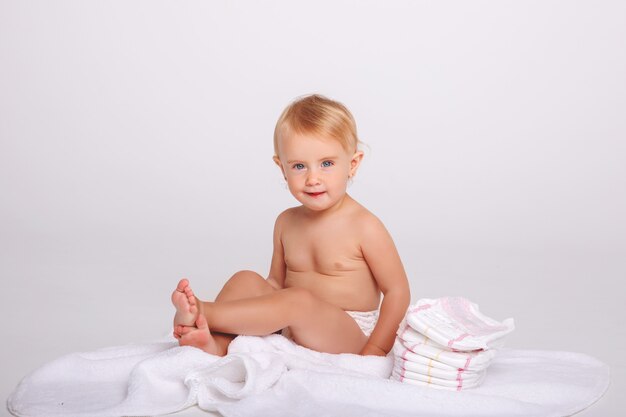 Baby girl in diaper playing with Teddy bear on white background.