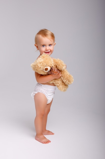 Baby girl in diaper playing with Teddy bear on white 