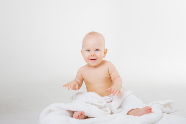 Baby girl in a diaper sitting wrapped in a towel isolated on a white background