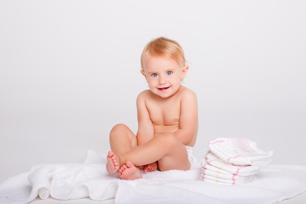 baby girl in a diaper with a stack of diapers on a white background