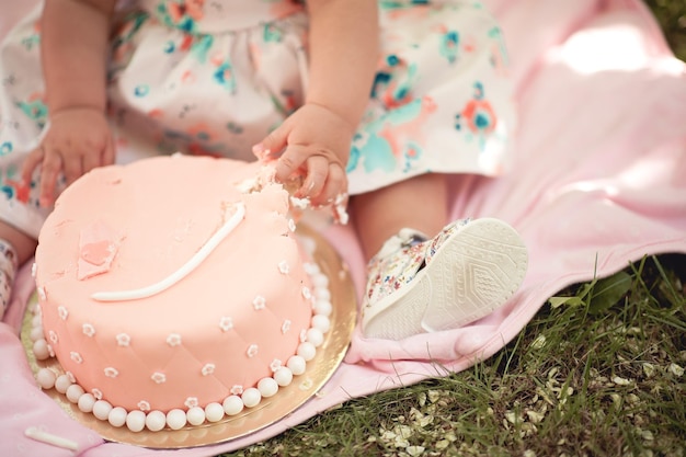 屋外でクリームチーズケーキを食べる女の赤ちゃん。最初の誕生日を祝う