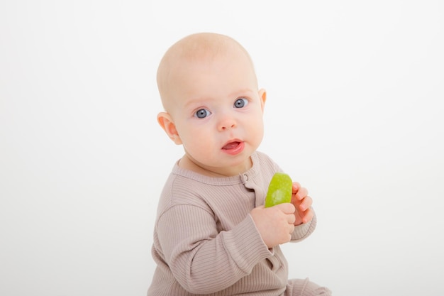 흰색 배경 스튜디오 촬영에 앉아 사과 한 조각을 먹는 아기 소녀