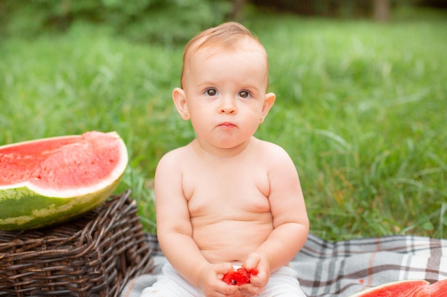 Baby girl eats watermelon in summer sitting on the lawn outside