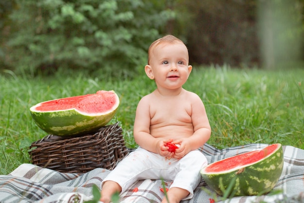 Baby girl eats watermelon in summer sitting on the lawn outside