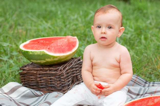 여자 아기는 여름에 야외 잔디밭에 앉아 수박을 먹는다