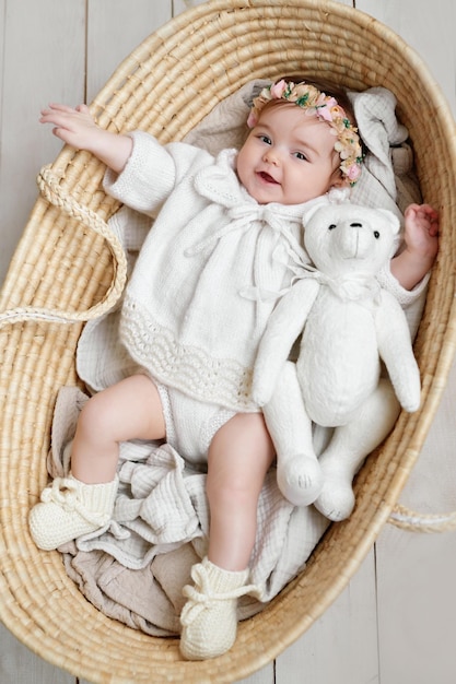 Baby girl in flower hat in wicker basket with wooden rattle Postcard Mother's Day and Easter Children Protection Day World Happiness Day Smiling child