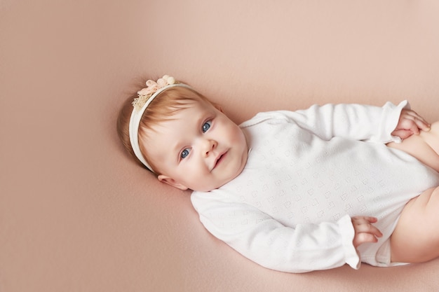 Baby girl of four months lies on a light pink wall