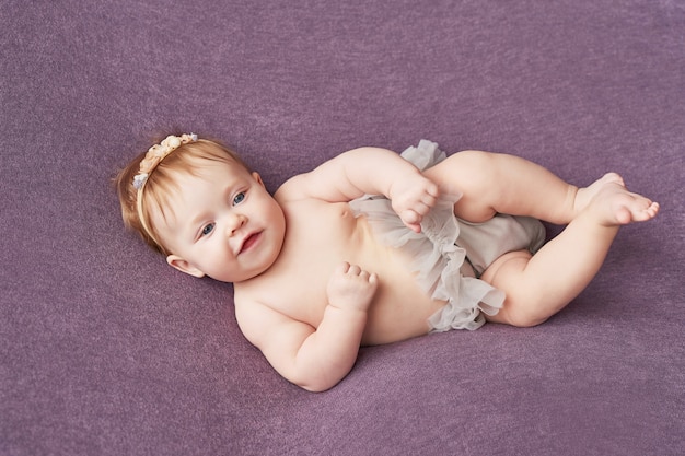 Baby girl of four months lies on a purple wall