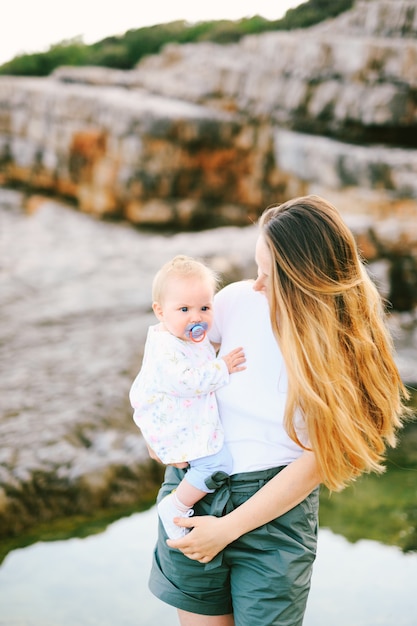 Baby girl in her mother's arms on a rocky beach