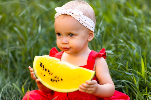 A baby girl hold in hands yellow watermelon.