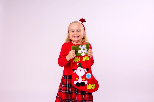 baby girl holding Christmas sock for gifts on white wall