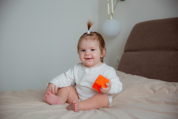 The baby girl is sitting at home on the bed in the bedroom playing with cubes