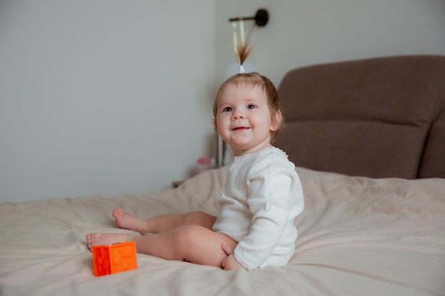 The baby girl is sitting at home on the bed in the bedroom playing with cubes