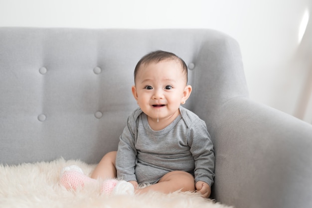 Baby girl is smiling and sitting on sofa in jumpsuit