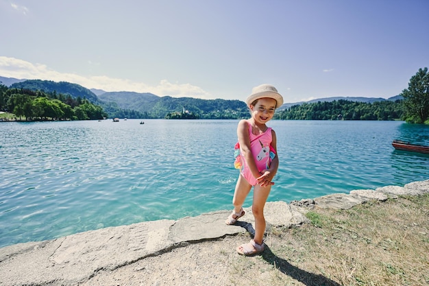 Baby girl is swimsuit and hat posed in pier of view beautiful Bled Lake Slovenia