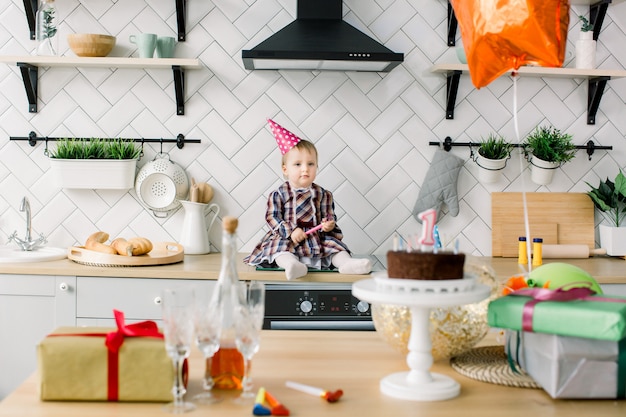 Bambina in cucina. il primo compleanno del bambino. bella bambina che celebra la festa di compleanno con palloncini e torta birtday. una festa di un anno. ragazza infantile sveglia in cappello rosa di compleanno.