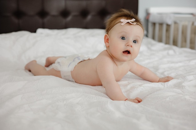 A baby girl laying on her stomach on a bed with a white diaper that says " i'm a baby ".