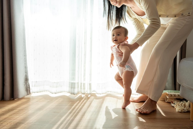 A baby girl learning first steps walk with mother family child childhood and parenthood concept