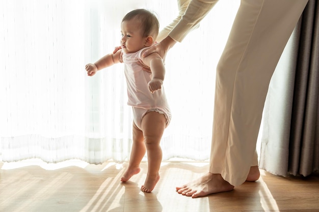 A baby girl learning first steps walk with mother family child childhood and parenthood concept