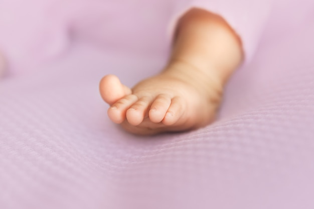 Baby girl leg on lilac fabric, tiny toes in a selective focus