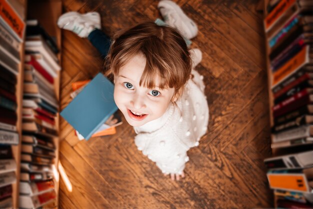 Bambina in biblioteca con libri in mano. bambino carino esplora gli scaffalihe