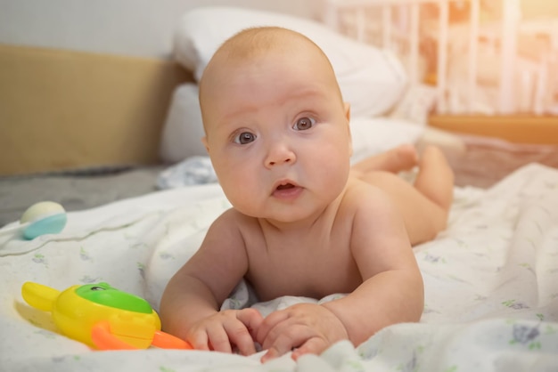 Baby girl lying on tummy on bed enjoys playing with toys