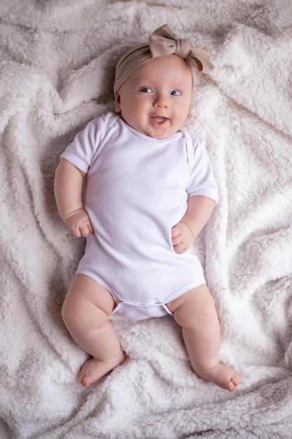 彼女の胃に白い服を着て白い毛布の上に横たわって、カメラを見て笑っている女の赤ちゃん赤ちゃんの朝の赤ちゃんのものの概念