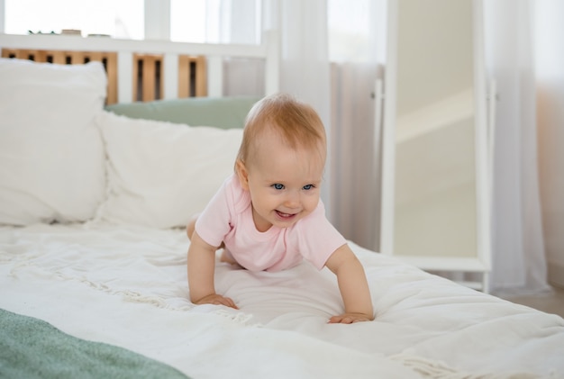 Baby girl in a pink bodysuit crawls on the bed in the room