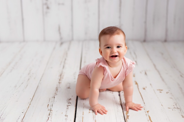 ピンクのボディースーツの女の赤ちゃんが床をクロールします。