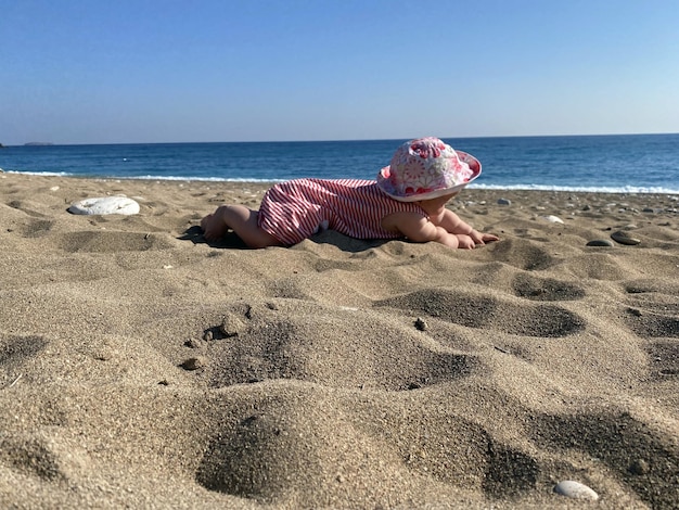 Фото Девочка играет на пляже в песке в детском купальнике и шапочке ползет ребенок ползет к воде на пляже
