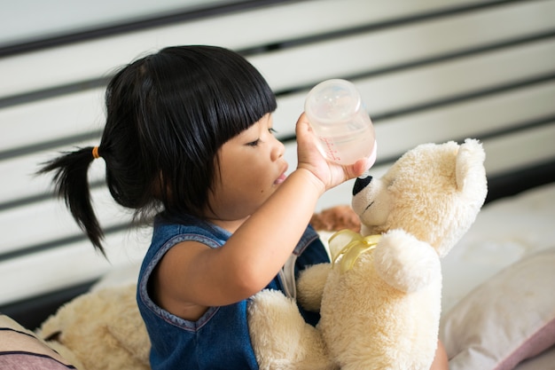 女の赤ちゃんがベッドの上で牛乳を飲むテディー・ベア