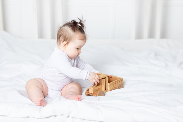 Baby girl playing wooden toy typewriter on the bed at home, the concept of play and development of children