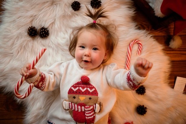 Baby girl in a red Christmas costume with retro garlands sits on a fur