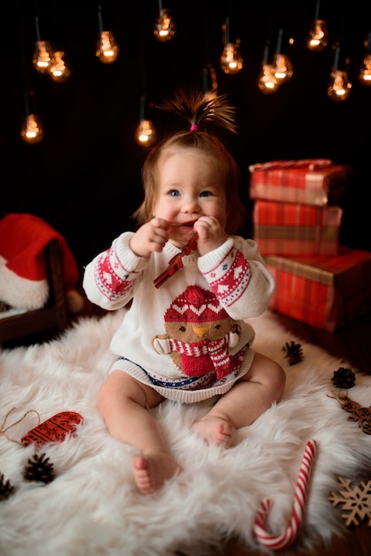 Baby girl in a red Christmas costume with retro garlands sits on a fur