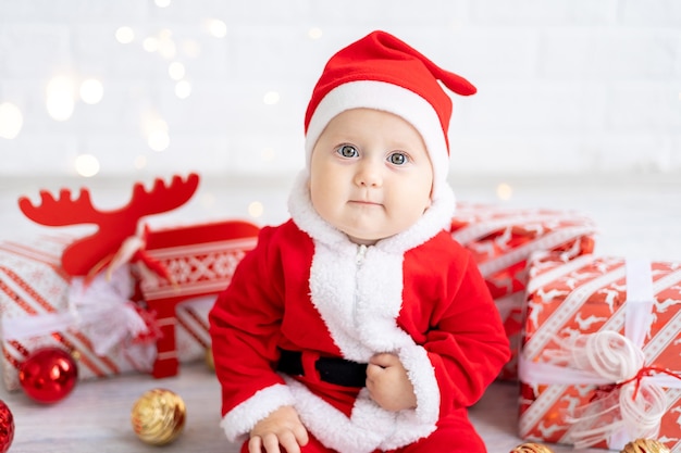 Una bambina con un costume rosso da babbo natale siede con scatole di regali e giocattoli di natale su uno sfondo bianco