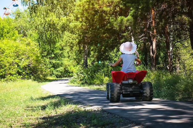 Baby girl riding on a red ATV in a green Park under the rays of the bright sun