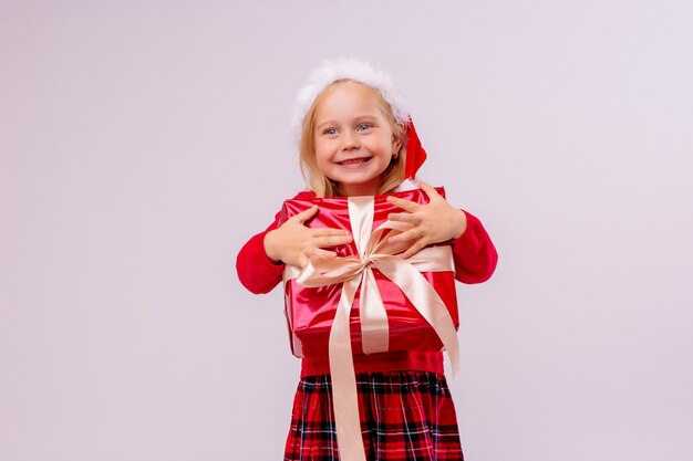 baby girl in Santa hat holding red gift box on white wall