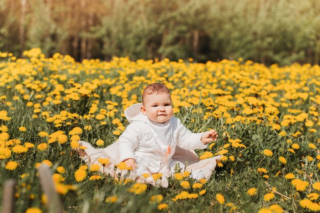 Photo baby girl sits on a field of dandelions on a sunny day