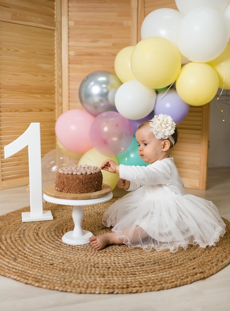 Baby girl sits on a mat and tries a cake on a stand