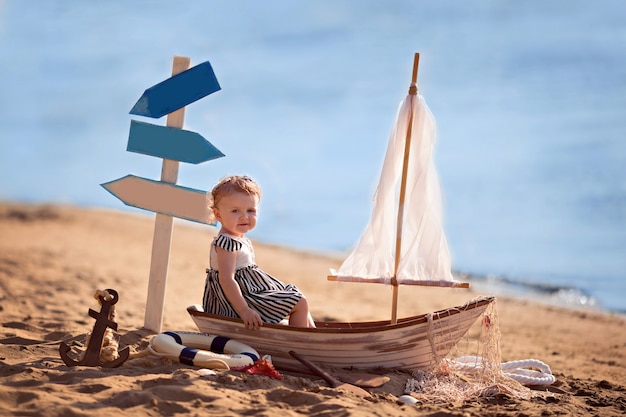 Baby girl sitting in a boat, dressed as a sailor, on a sandy beach