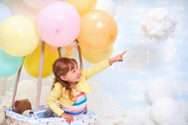 Baby girl sitting on a cloud next to a basket of balloon in the clouds