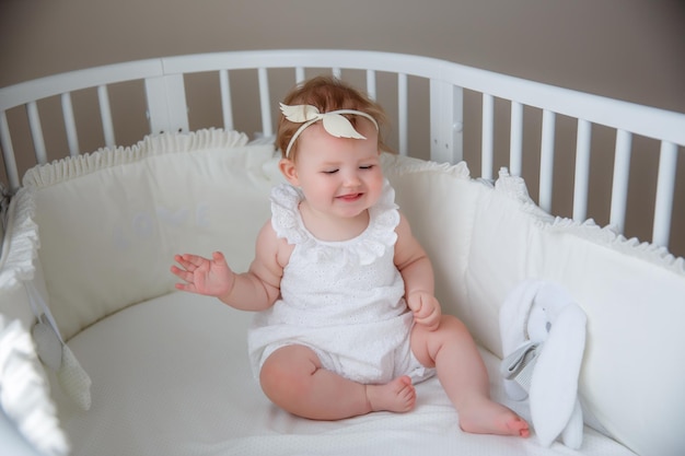 baby girl sitting in a crib in a white bodysuit