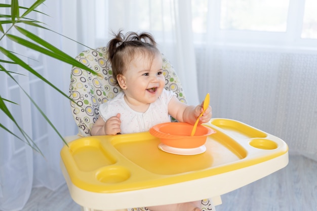 Baby girl sitting in a high chair and laughing, baby food concept