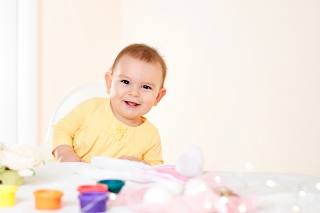 Baby girl sitting at the table and painting holiday easter eggs smiling happy childhood