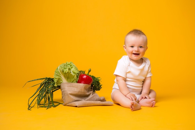 Baby girl sitting with bag of vegetables on yellow 