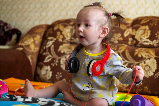 Photo baby girl sitting with headphones on bed at home